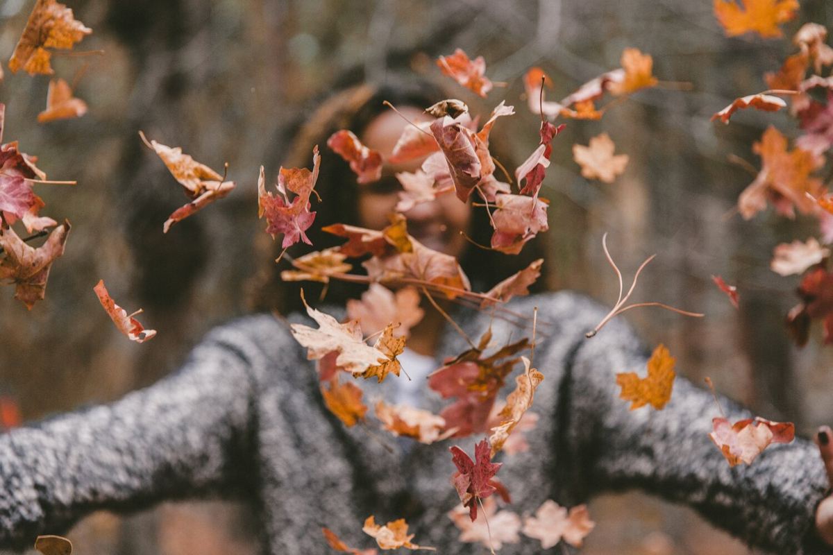 A woman tossing autumn leaves into the air