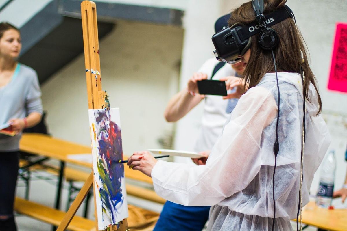 A woman wearing a VR headset while painting at an easel